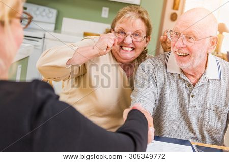 Senior Adult Couple Celebrating Over Documents in Their Home with Agent At Signing.