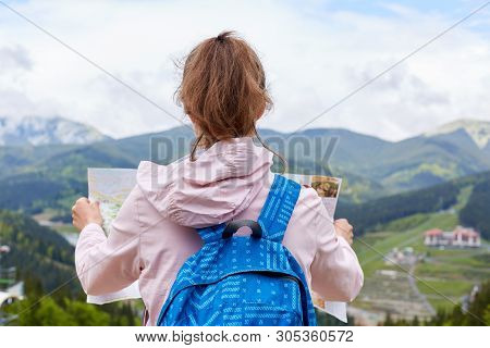Back View Of Travel Standing At Top Of Hill Holding Map With Current Route To Move On, Looking At Ma