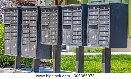 Panorama Row Of Cluster Mailboxes With Numbered Compartments On A Sunlit Sidewalk