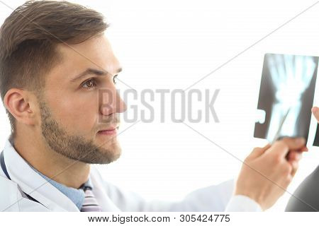 Portrait Of Physician Holding X-ray Picture And Talking About Injury With Visitor. Bearded Serious D