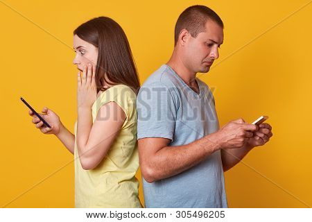 Shocked Emotional Woman Standing Back To Back To Man, Touching Her Cheek With Hand, Holding Mobile P