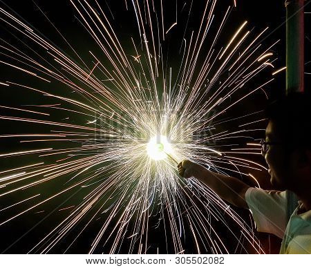A Man Holding Hand Charki, A Hand Firework Emitting Circular Sparks In Black Background