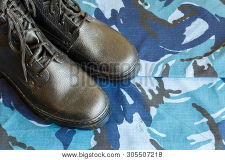 A Pair Of Black Army Boots On Fabric With Blue Camouflage With Copispace For Text.
