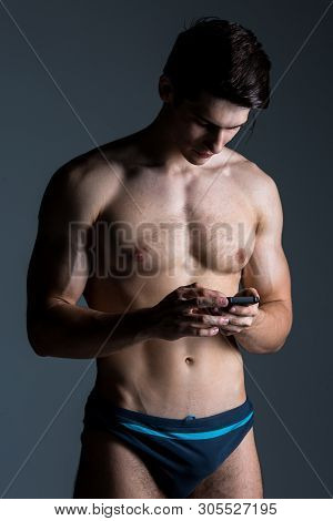Low Key Portrait Of Muscular Shirtless Man At Dark Background Standing With Smart Phone