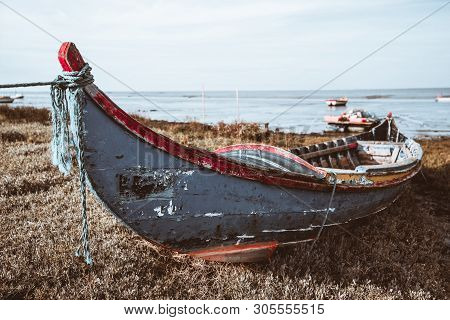 An Old Peeling Colorful Wooden Rope-bound Fishing Boat On The Grass Of The River Bank With A Horizon