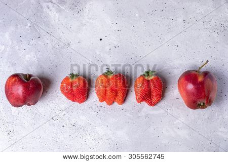 Ugly Two Apples And Three Strawberries Are Lying In Row On Grey Concrete Background.