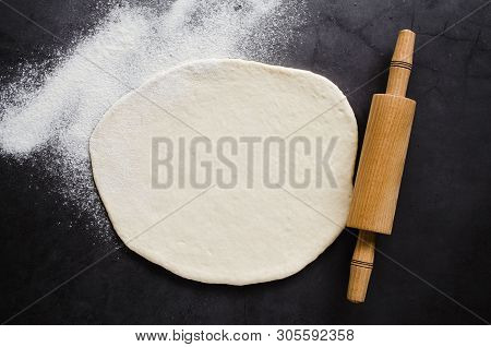 Rolled Dough, Baking Flour And Rolling Pin On A Dark Blackboard. Place For Text Or Recipe