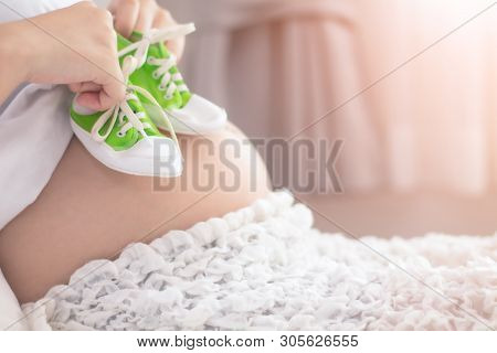 Small Shoes For The Unborn Baby In The Belly Of Pregnant Woman. Pregnant Woman Holding Small Baby Sn