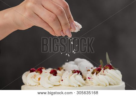 The Condater Sprinkles The Cake With Grated Almonds And Coconut. Close-up Of A Hand And Pouring Crum