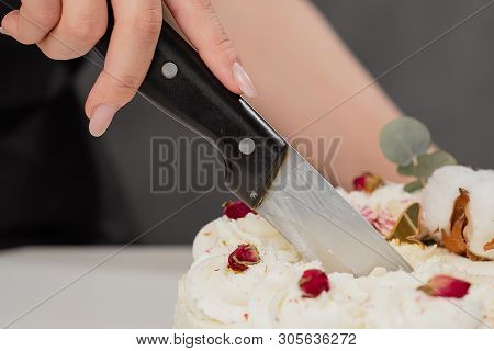 A Condater Cuts A Beautiful Fresh Decorated White Cake With A Large Knife.