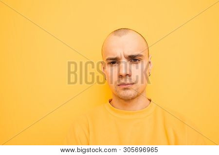 Close Portrait Of An Unhappy Original Guy In Stylish Clothes On A Yellow Background. Mirthless Young