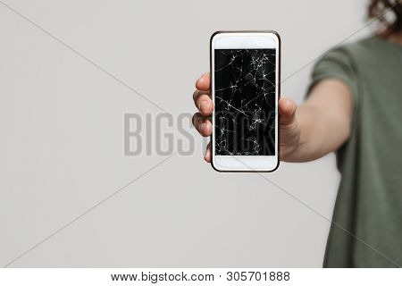 Close Up, Hand Holding Broken Smartphone With Damaged Screen Protection Isolated On Gray Background.