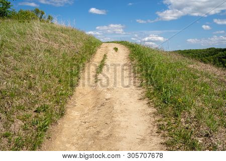 Dirt Hiking Trail Surrounded By Green Grass Goes Up A Hill On A Sunny Day, Leading Lines