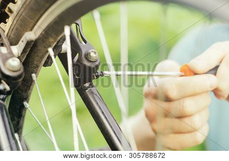 A Man Unscrews The Bolts With A Screwdriver On The Mount Wheel Brakes Of A Mountain Bike On The Back