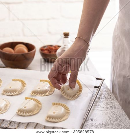 Woman put empanadillas , small filling tuna pies in roasting tray  to baked pastry in oven. Typical 