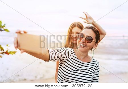 Two Girlfriends Posing For Selfie On The Sea Side Using Smartphone