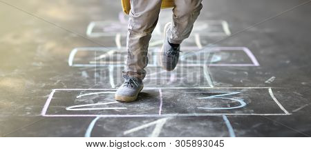 Closeup Of Little Boy's Legs And Hopscotch Drawn On Asphalt. Child Playing Hopscotch Game On Playgro