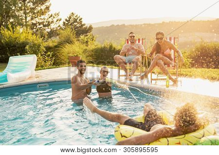 Group Of Friends At A Poolside Summer Party, Having Fun In The Swimming Pool, Drinking Beer And Spla