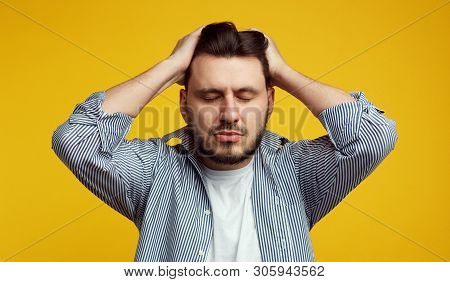 Upset Young Man Keeps Both Hands On Head, Closes Eyes, Suffers From Migraine, Has Sad Fatigue Facial