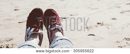 Feet Of Young Woman In Sport Footwear And Jeans Relaxing After Hiking On Sand Beach. Pov. Adventure 
