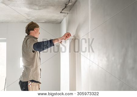 Worker Applies A Sheet Of Wallpaper. Man Glueing Wallpapers On Concrete Wall. Repair The Apartment. 