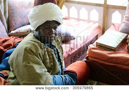 Moscow, Russia - June 2019: Black Man In A Turban Sits In A Room Decorated In Oriental Style During 