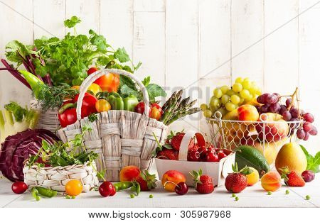 Still life with various types of fresh vegetables, fruits and berries in baskets on a white wooden table. Concept of healthy eating.