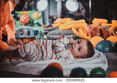Happy Smiling Cute Toddler Is Lying On The Special Table Surrounded By Ortopedic Toys While Expirien