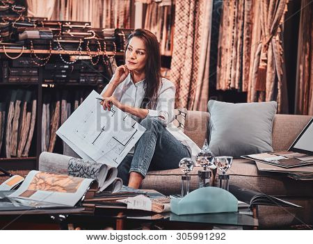 Attractive Pensive Woman Is Sitting On The Sofa At Her Curtians Atelier While Handing Drawings About