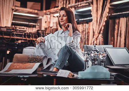 Attractive Pensive Woman Is Sitting On The Sofa At Her Curtians Atelier While Handing Drawings About