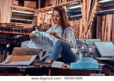 Attractive Pensive Woman Is Sitting On The Sofa At Her Curtians Atelier While Handing Drawings About