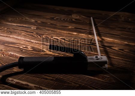 Welding Electrode Holder With Electrode On A Wooden Background. Studio Photo In Hard Light.