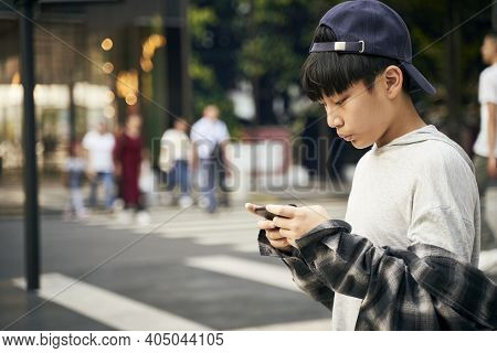 Teenage Asian Child Looking At Cellphone While Walking On Street