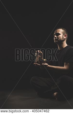 Young Caucasian Man Sitting Playing The Tibetan Singing Bowll In Black Clothes On Black Background.