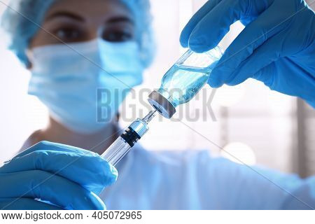 Woman Filling Syringe With Vaccine From Vial On Blurred Background, Closeup
