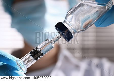 Woman Filling Syringe With Vaccine From Vial On Blurred Background, Closeup