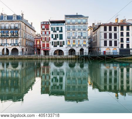 Old traditional building facades and their reflections in the Nive River at sunrise in Bayonne, France.