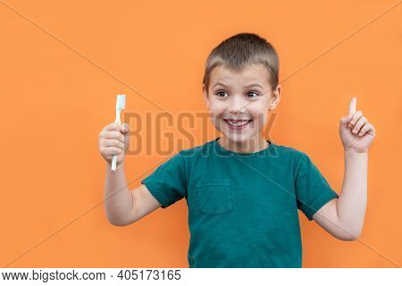 Boy Without Milk Upper Tooth In Green T-shirt Holds Toothbrush In Hand On The Orange Background.
