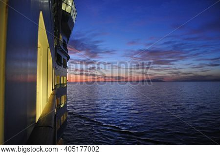Lights On Cruise Ship Moving Through Water As Sun Sets.