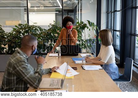 Diverse group of business people working in creative office. group of people wearing face masks and using laptops. social distancing protection hygiene in workplace during covid 19 pandemic.
