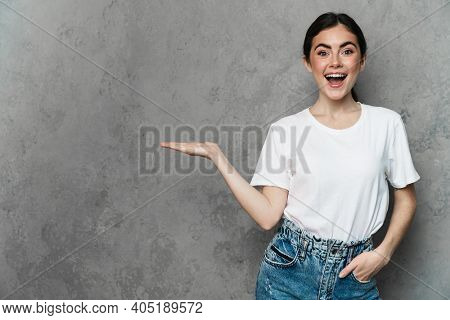 Portrait of cheerful young woman prsenting copy space while standing over isolated background