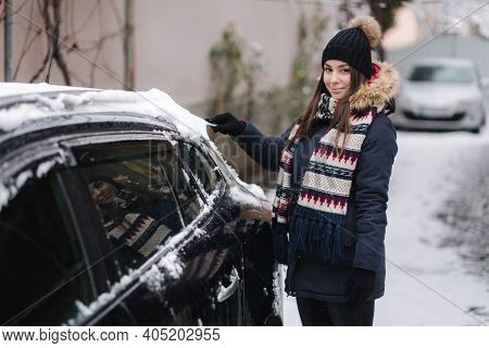 A Woman Is Cleaning Snowy Window On A Car With Snow Scraper. Pretty Woman Warmy Dressed Clean Her Ca