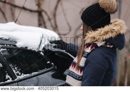 A Woman Is Cleaning Snowy Window On A Car With Snow Scraper. Pretty Woman Warmy Dressed Clean Her Ca