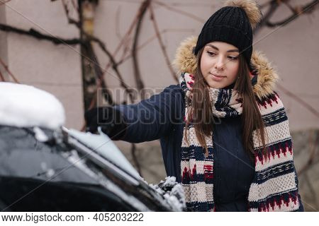 A Woman Is Cleaning Snowy Window On A Car With Snow Scraper. Pretty Woman Warmy Dressed Clean Her Ca