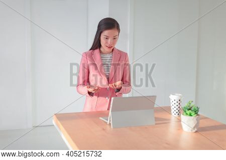 Videoconference online presentation Asian business woman talking teaching live webinar from home office streaming from laptop on standing desk explaining with gestures.