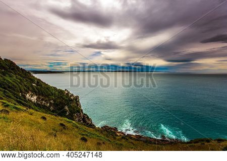 The picturesque coast of the Pacific Ocean near Cape Nugget. Sunset sky portends a storm. South Island, New Zealand. The concept of active, environmental and photo tourism