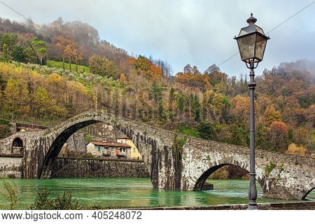 Picturesque stone Devil's Bridge over the Serchio River. Medieval bridge of magnificent architecture built a thousand years ago. Cold windy winter day. Travel to fabulous Italy. Province of Tuscany. 