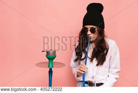 A Young Woman In A Hipster Image Smokes A Hookah, Sheesha And Enjoys Smoking.