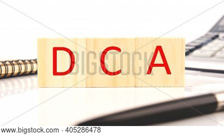 The Word Dca On Wooden Cubes On Cubes On A White Background Near A Pen, Calculator, Notepad.