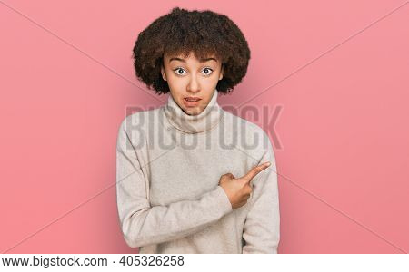Young hispanic girl wearing wool winter sweater pointing aside worried and nervous with forefinger, concerned and surprised expression 